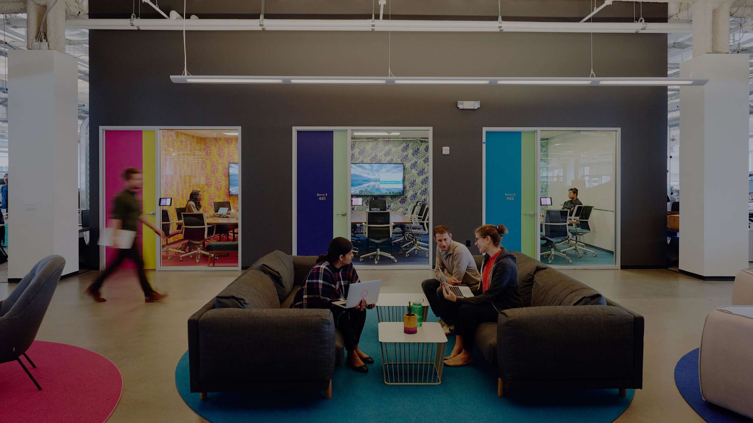 Image of Lyft employees sitting on two couches facing each other in Lyft office with conference rooms in the background.