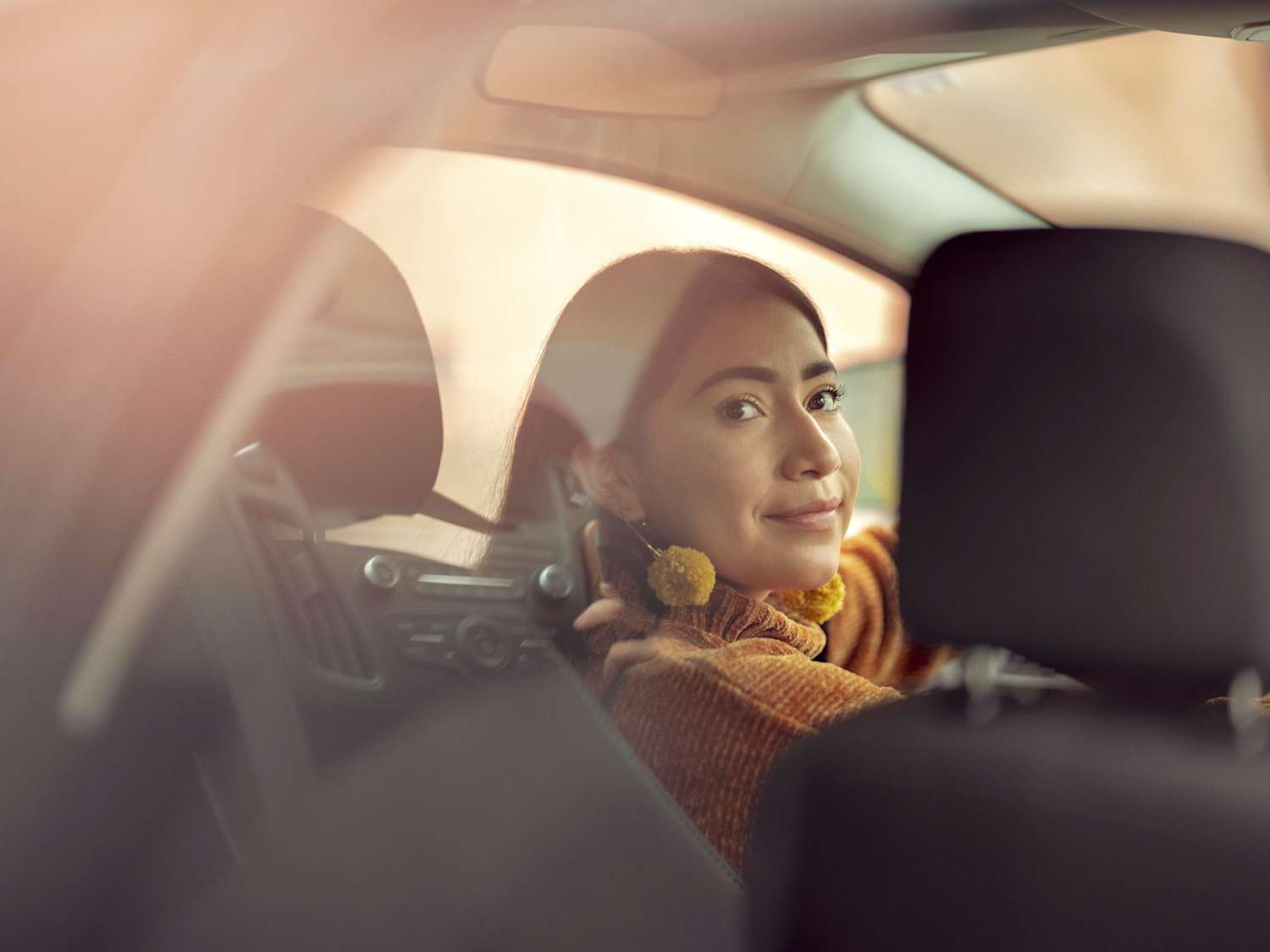 A female Lyft Driver smiling back at a passenger from the driver's seat.