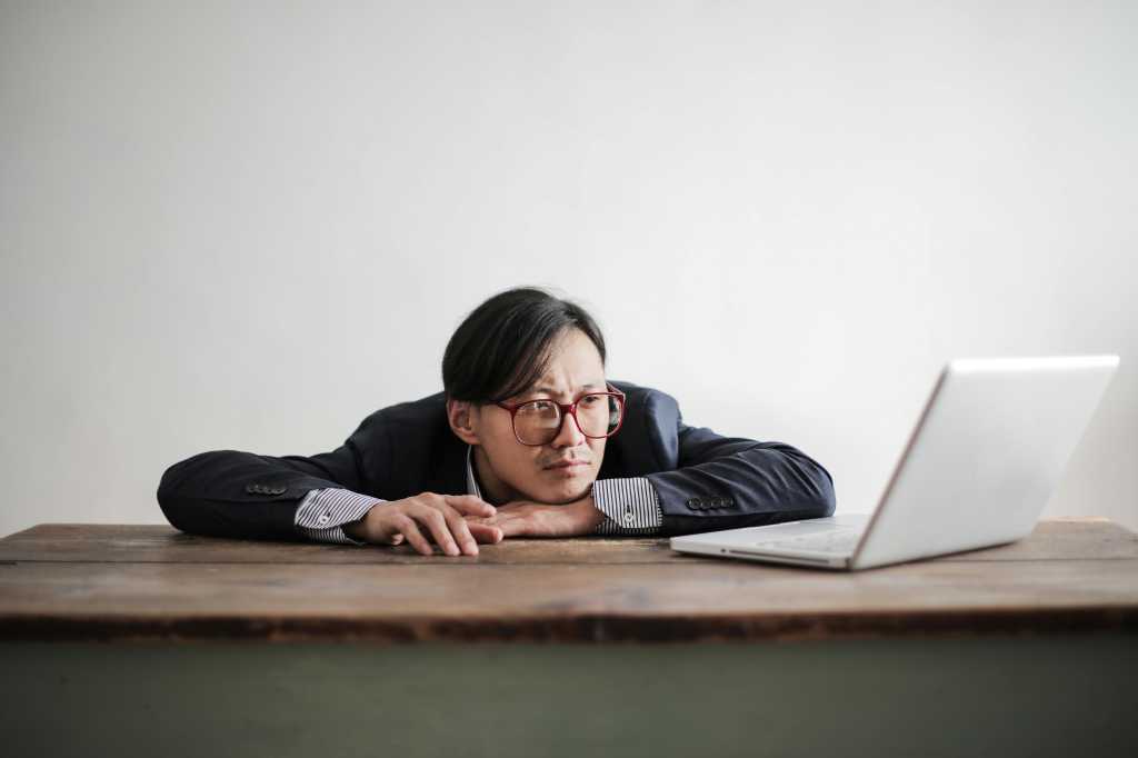 Man with short hair and glasses staring at computer with chin on desk