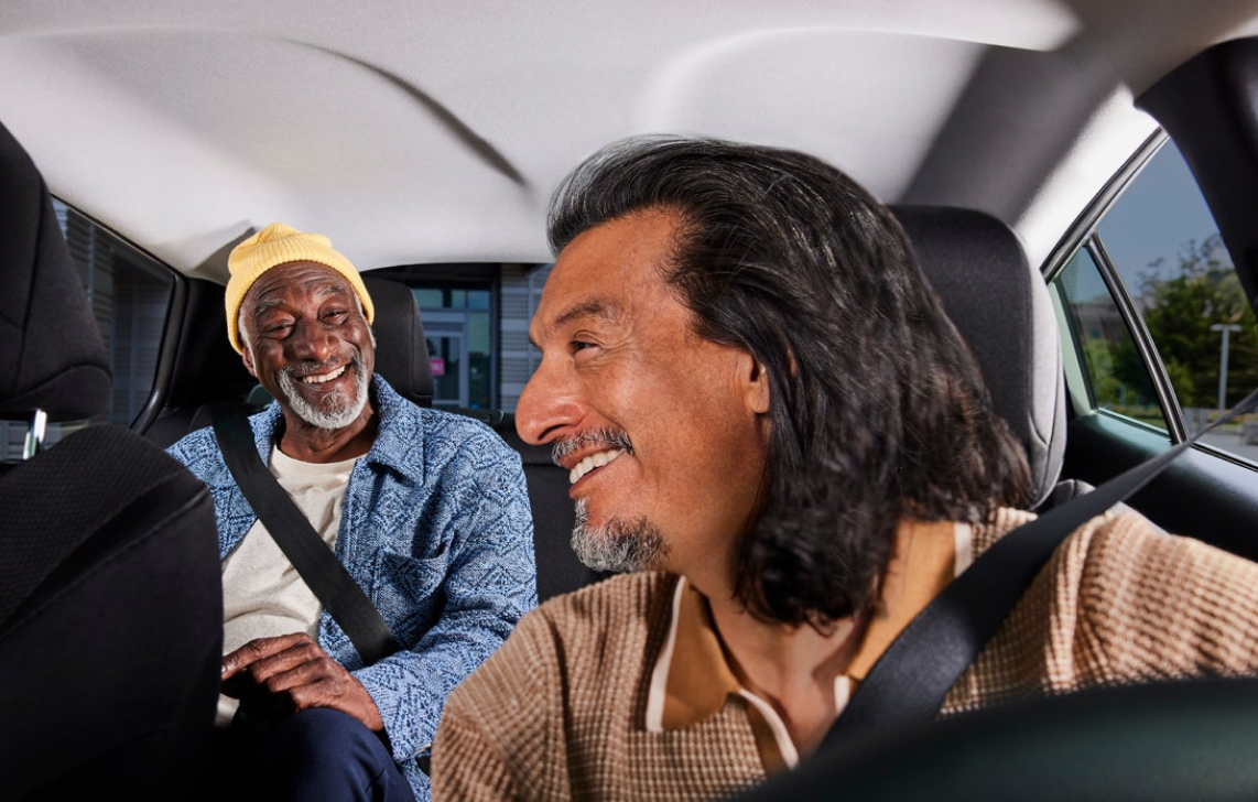 Image of smiling driver looking back at a smiling passenger in a car.