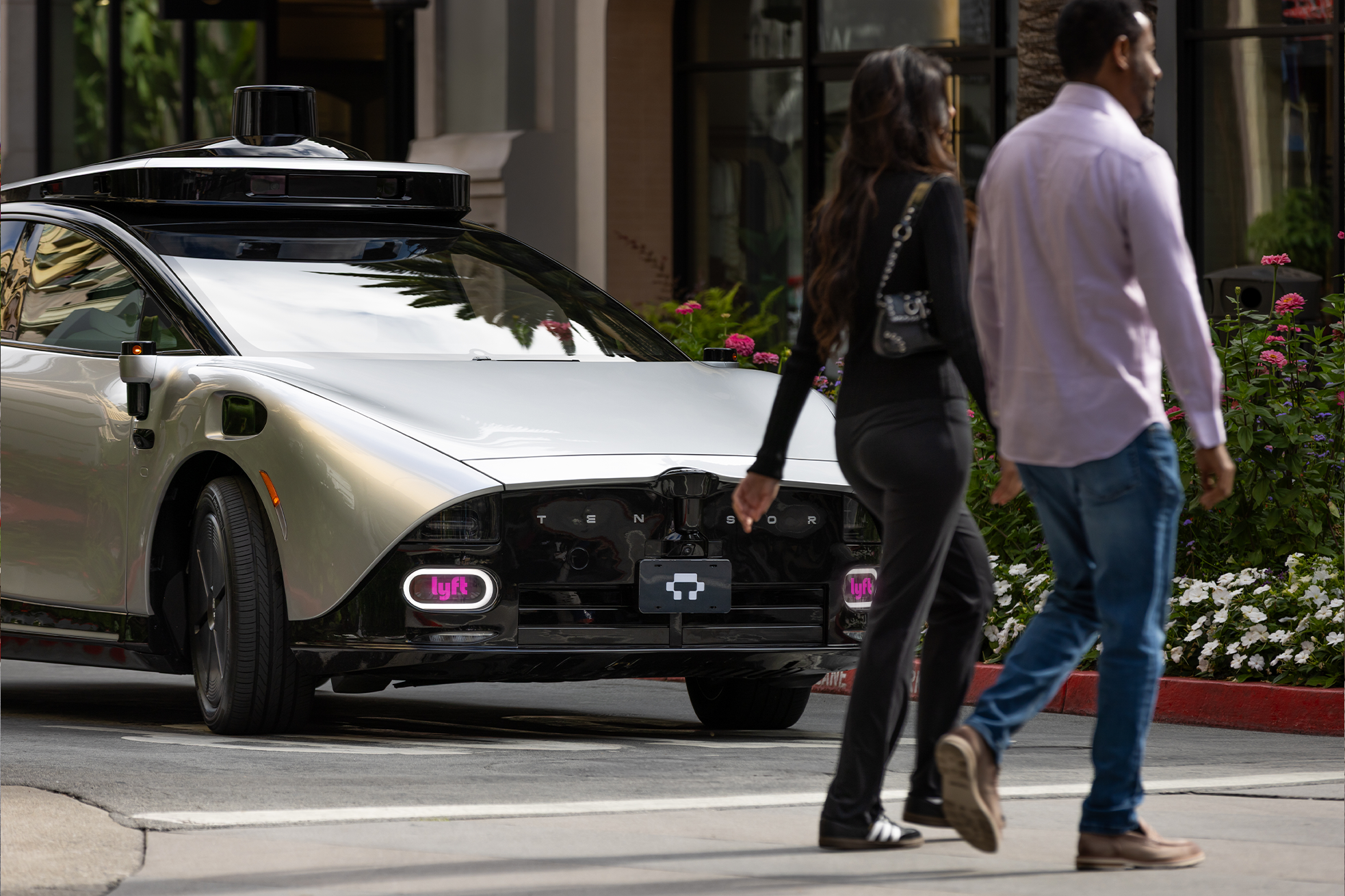Image of the front of Lyft Tensor Robocar stopped in front of two people walking across a crosswalk.  